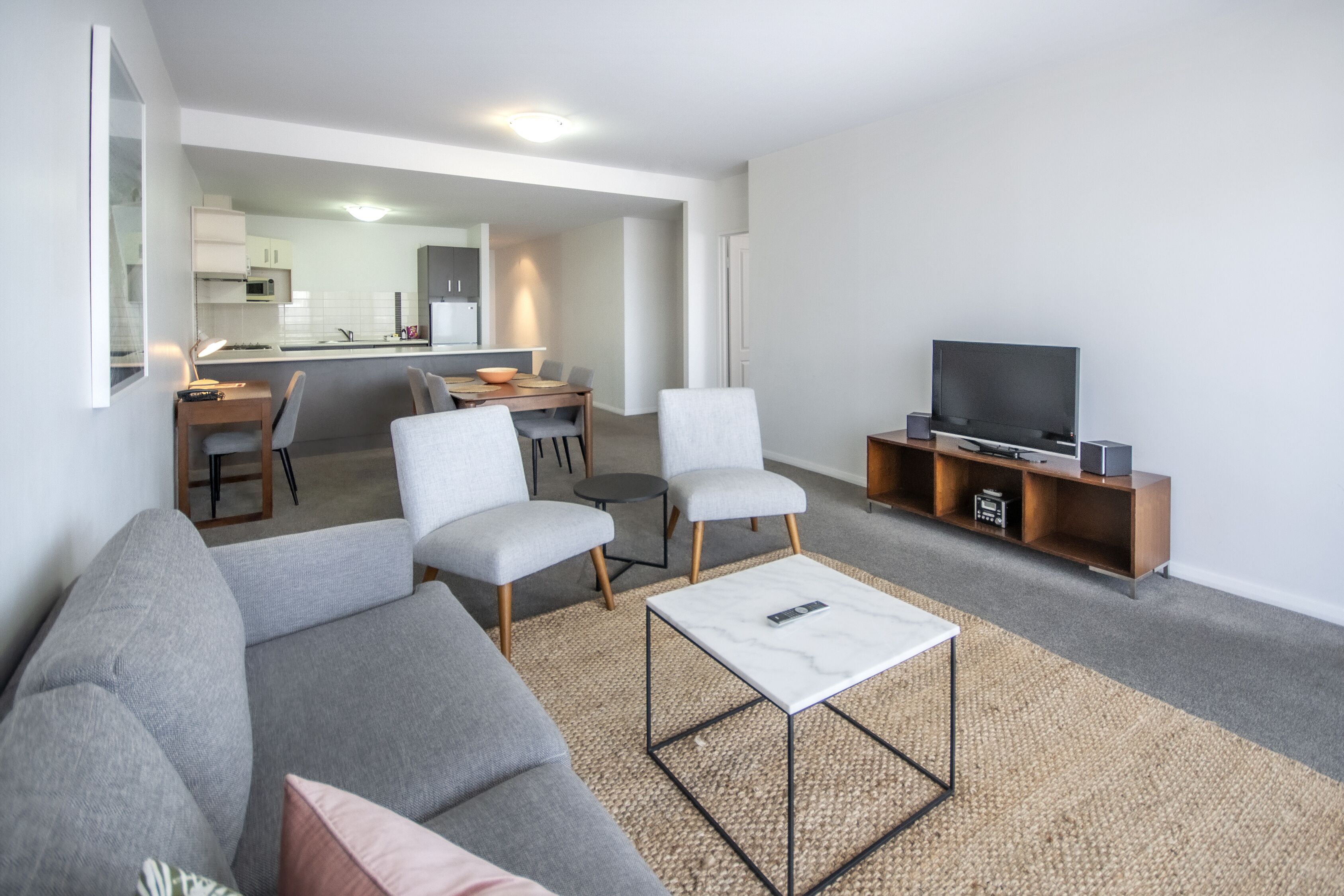 A modern living room with a grey sofa, two armchairs, a coffee table, and a TV on a wooden stand.