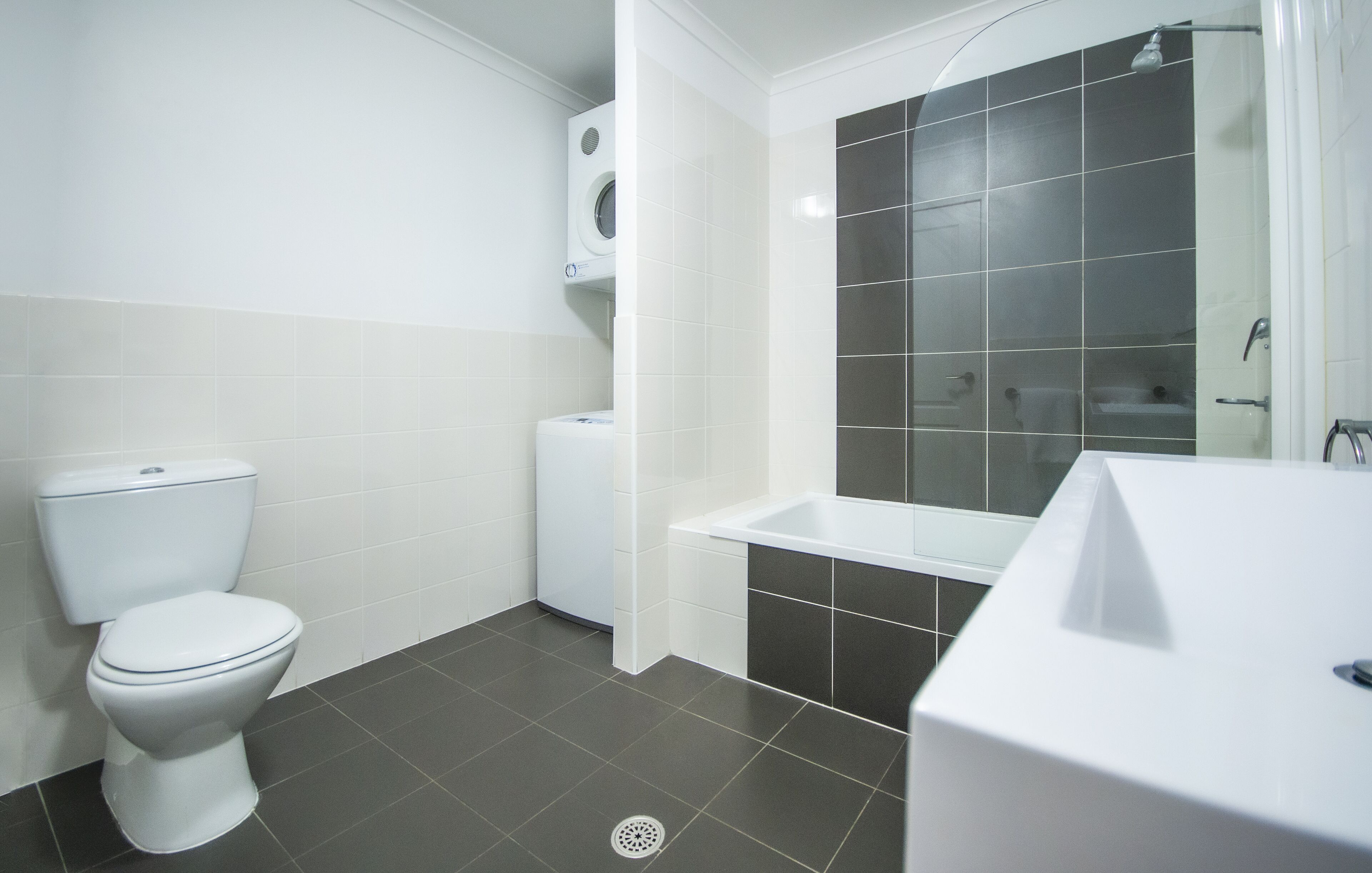 A bathroom with a toilet, a washing machine, a bathtub, and a sink.