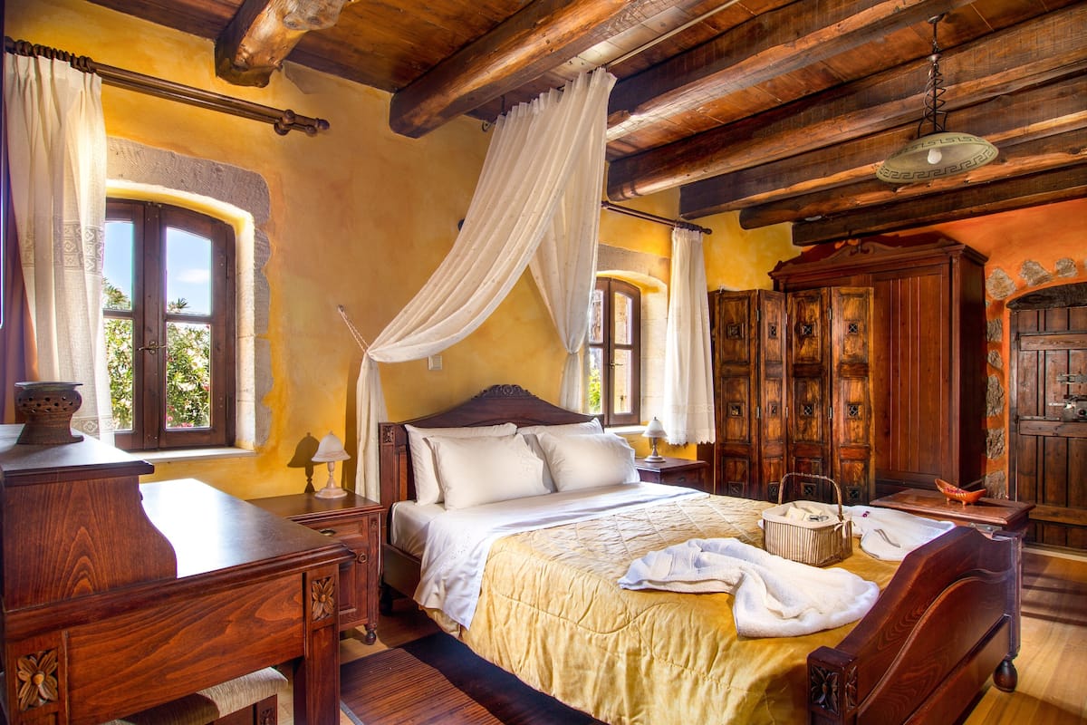 A traditional bedroom with a large bed, wooden furniture, and a window with curtains.