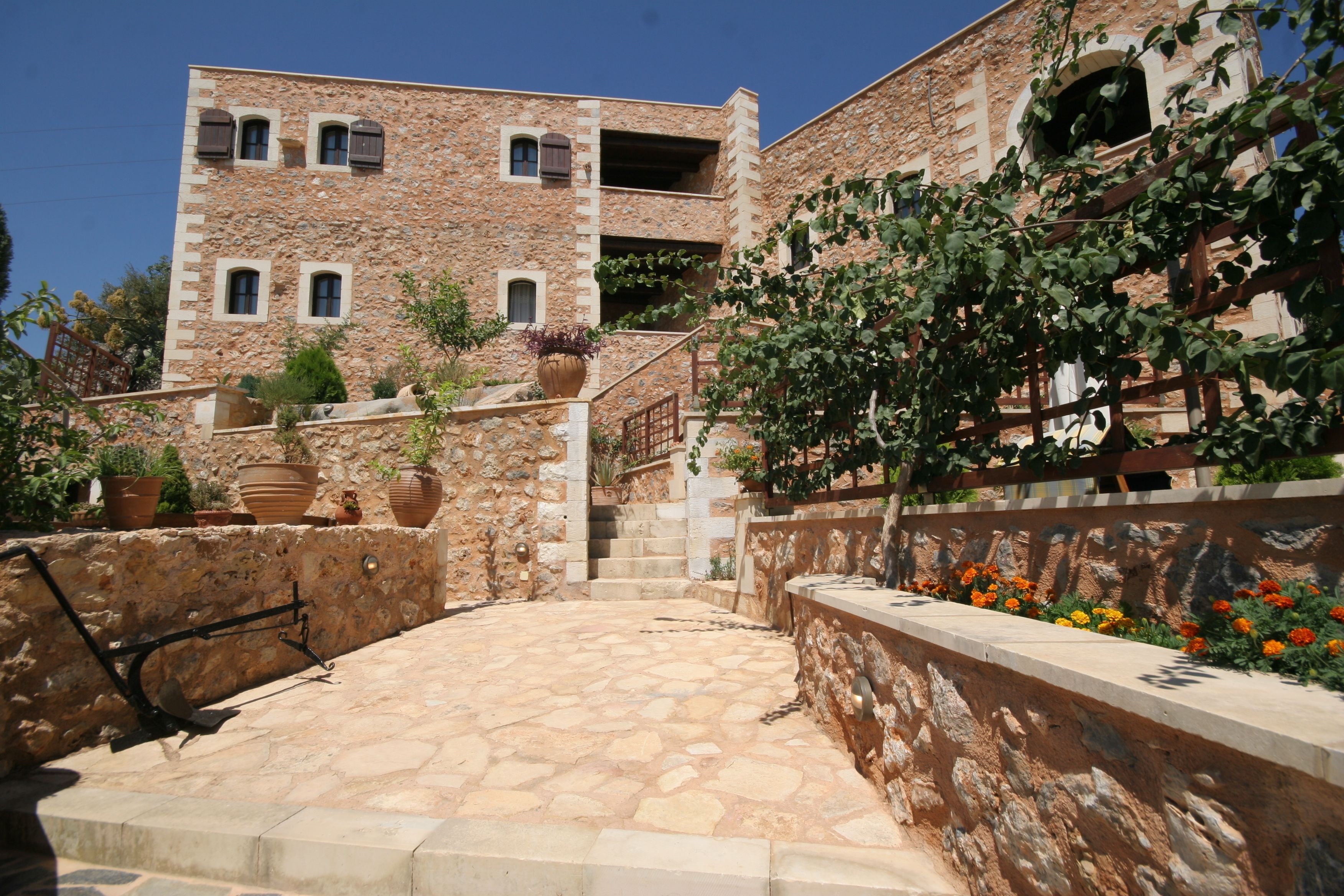 A stone building with a courtyard, potted plants, and a staircase leading to an upper level.