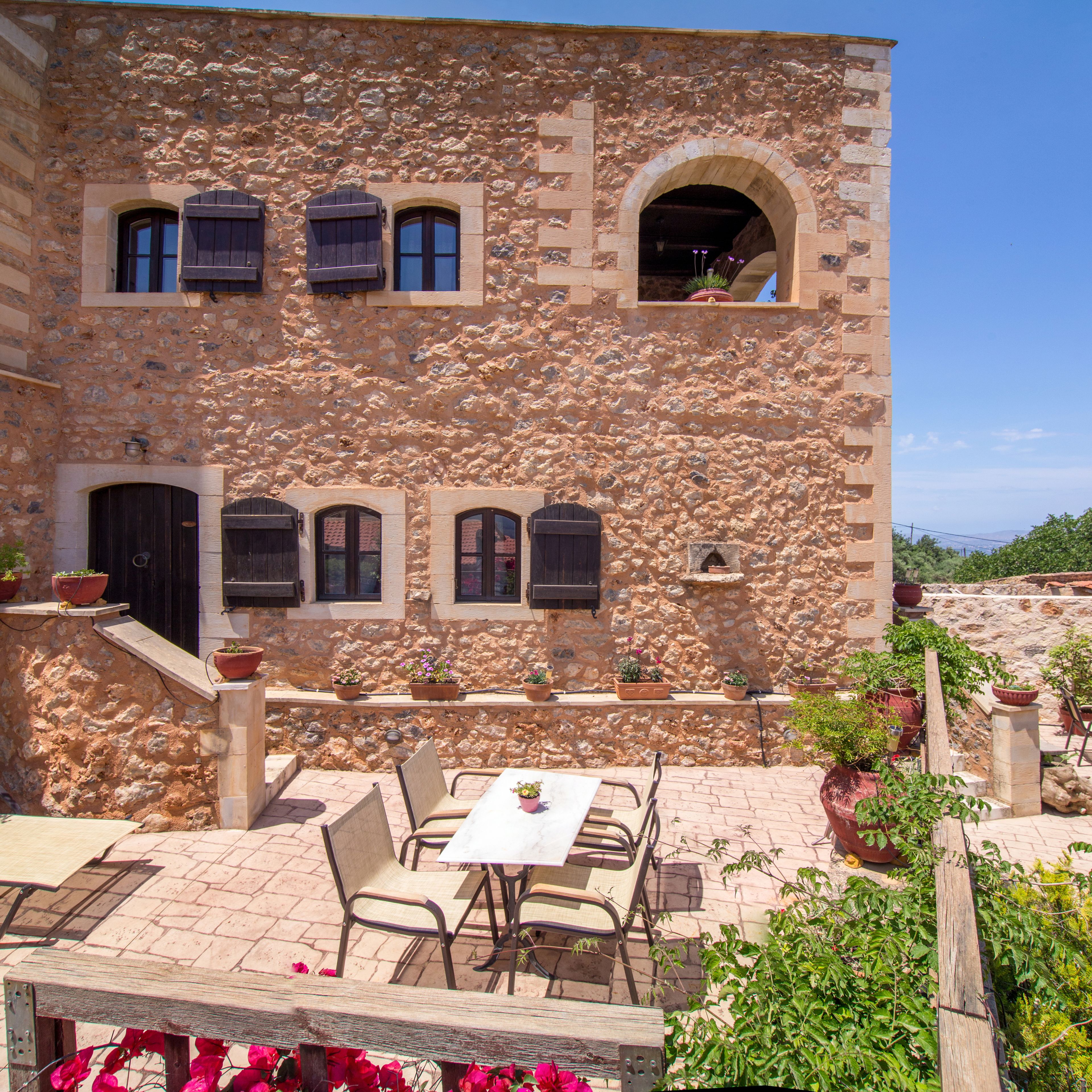 A stone building with a terrace, outdoor seating, and potted plants.