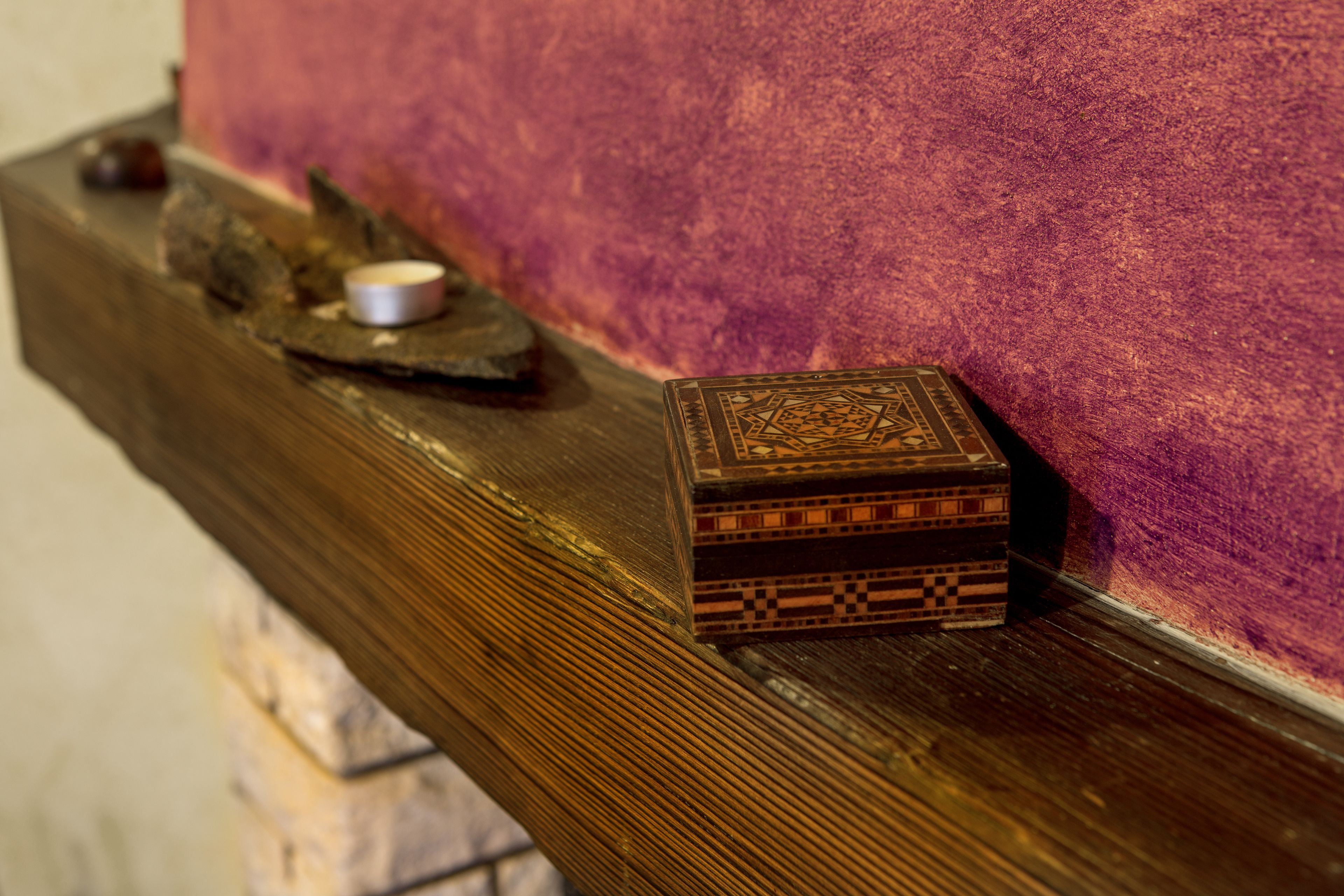 Una caja de madera pequeña y ornamentada, con diseños intrincados, sobre un estante de madera frente a una pared morada texturizada.