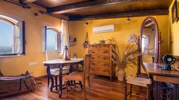 A room with wooden floors, a wooden table, a chair, a dresser, a mirror, and a window with curtains.