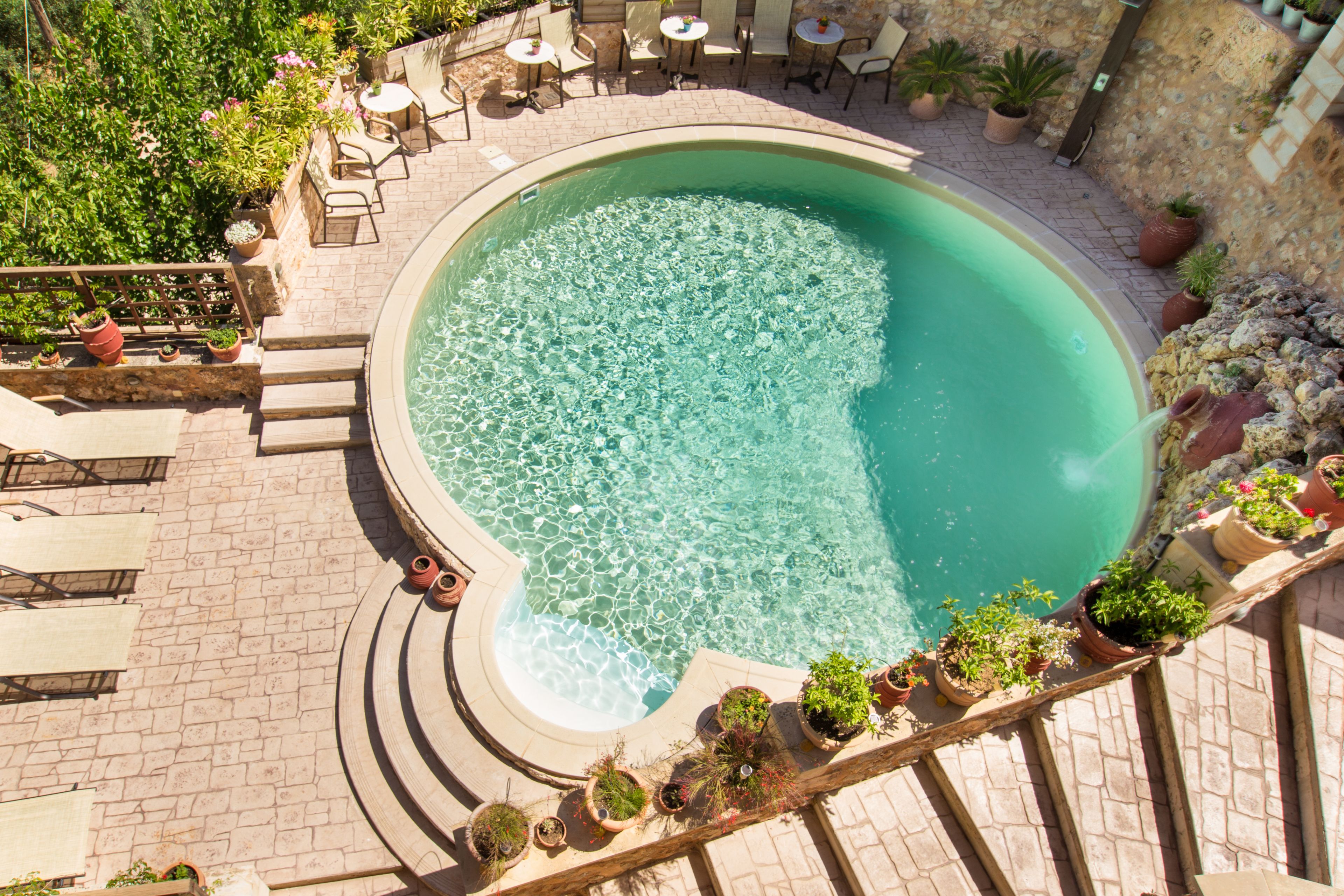 A circular pool with clear water, surrounded by a stone deck and potted plants.