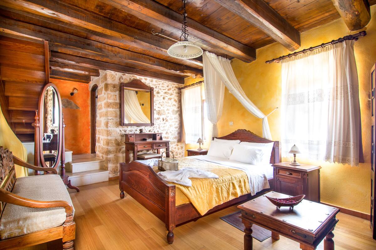 A traditional bedroom with a wooden bed, a nightstand, a bedside table, a chair, and a stone wall.