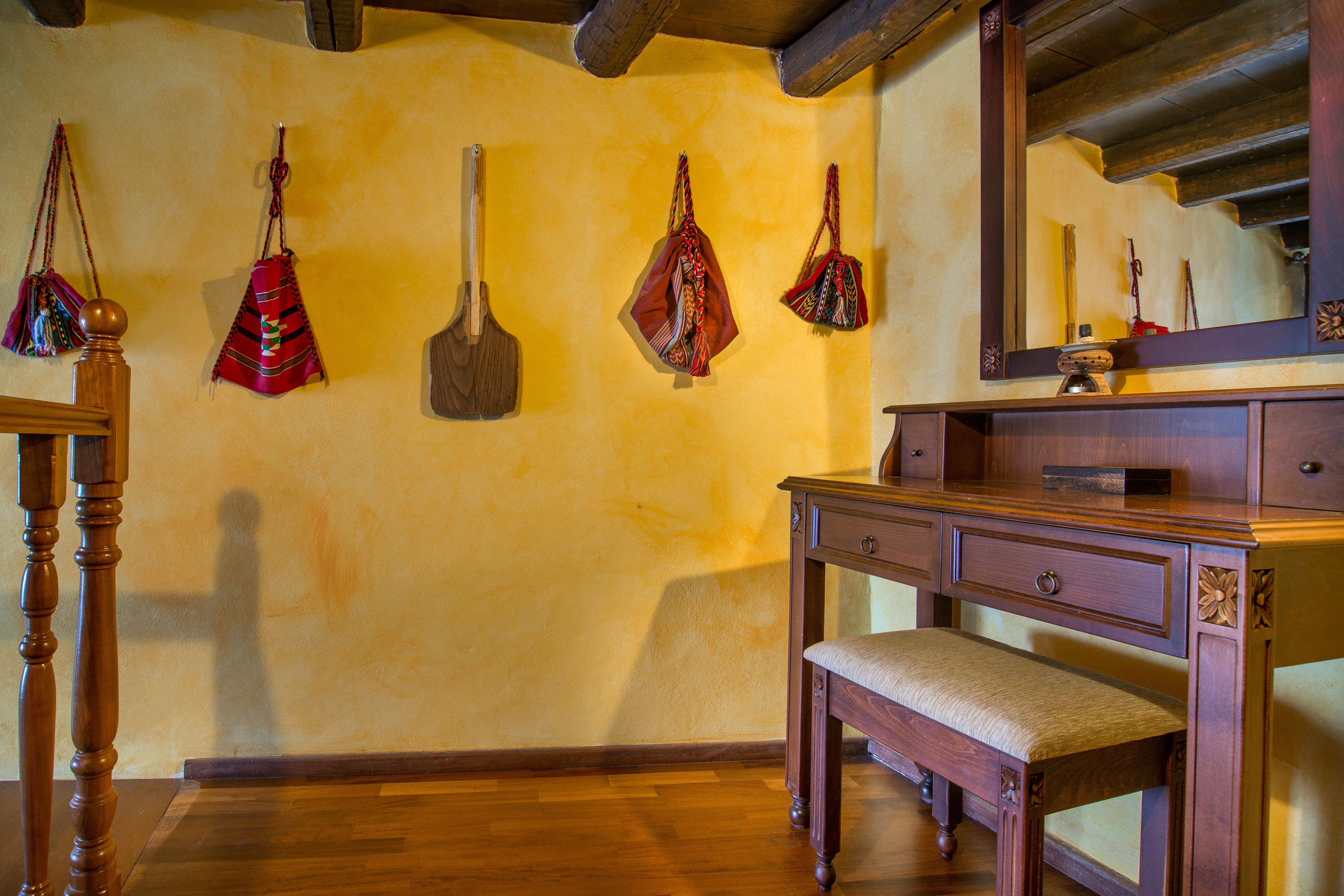 A wooden bench, a wooden dresser, and a mirror in a room with wooden floors and a yellow wall.