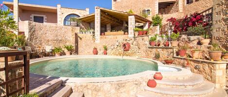 A courtyard with a swimming pool, stone steps, and potted plants.