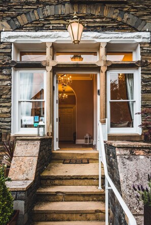 A stone building entrance with a chandelier, steps, and a door leading inside. - Wheatlands Lodge - Bed & Breakfast (Windermere)