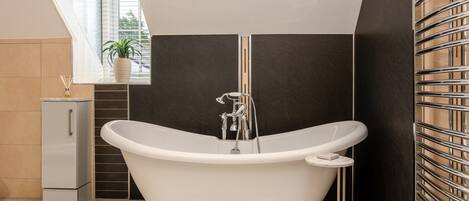A modern bathroom with a freestanding bathtub, a small cabinet, and a window with a plant.