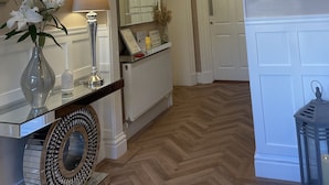 A hallway with a chandelier, a mirror, a radiator, and a door. - Wheatlands Lodge - Bed & Breakfast (Windermere)