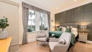 A bedroom with a large bed, two armchairs, a nightstand, a window with curtains, and a plant. - Wheatlands Lodge - Bed & Breakfast (Windermere)