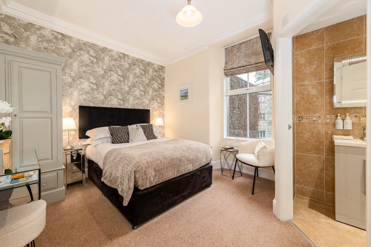 A bedroom with a large bed, bedside tables, a chair, a desk, and a window with a view.