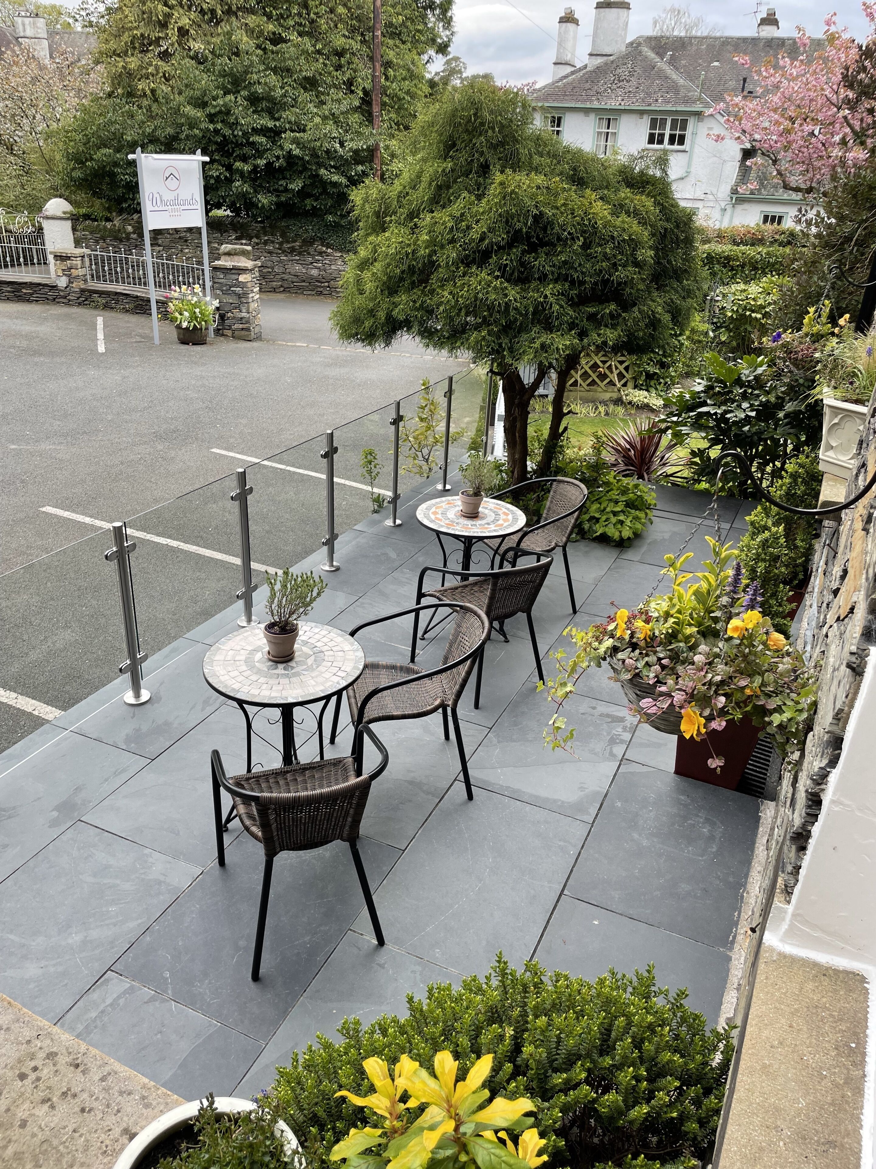 Een terras buiten met tafels en stoelen, omringd door potplanten en een stenen muur.