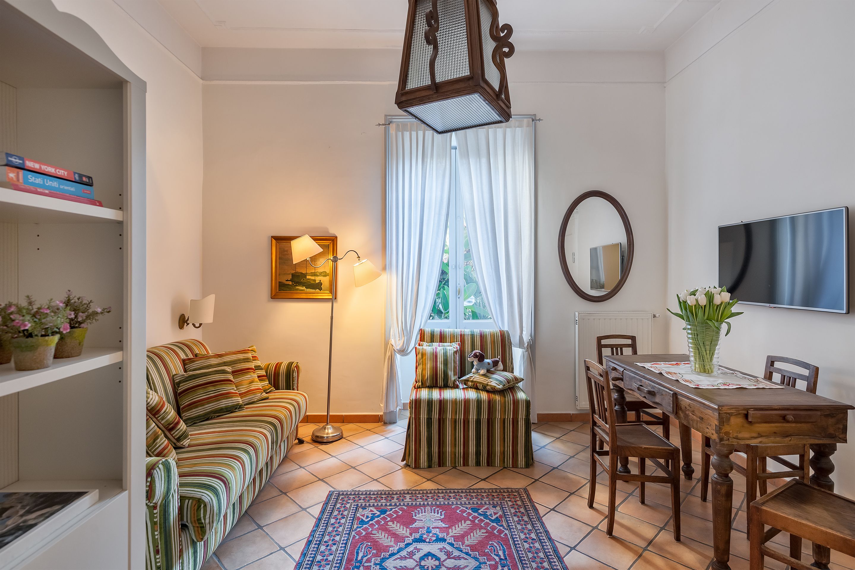 Ein gemütliches Wohnzimmer mit einem gestreiften Sofa, einem Esstisch mit Stühlen, einer Stehlampe und einem Fernseher an der Wand.
