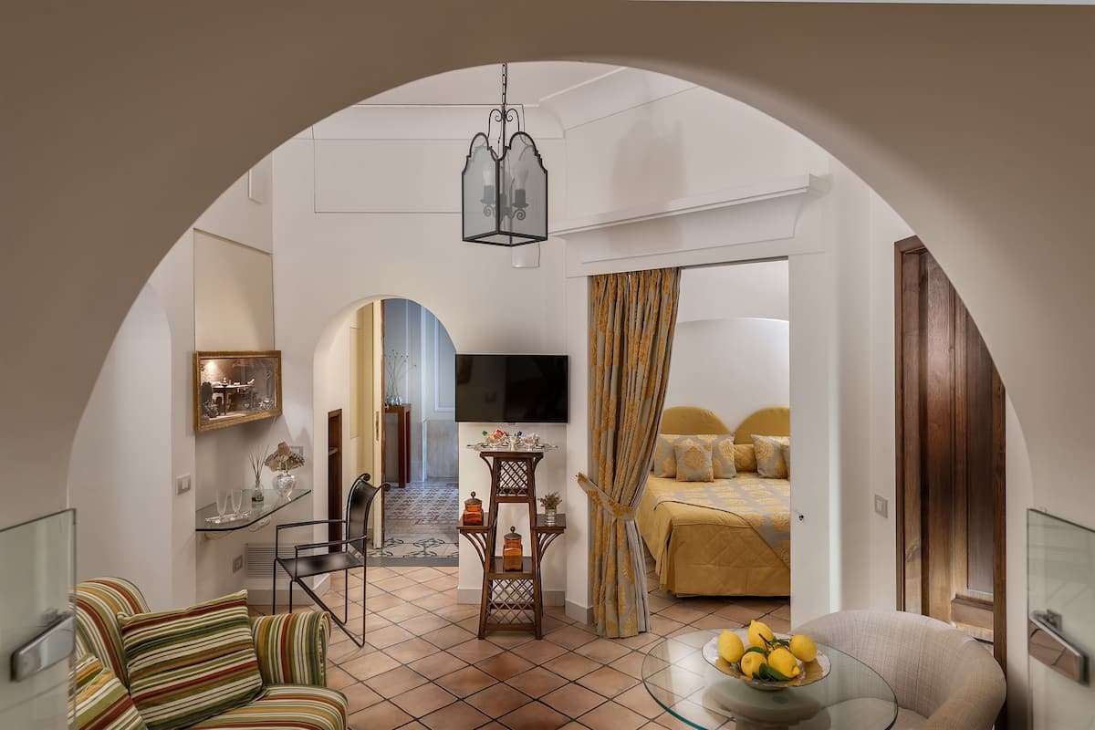 A hotel room with a dining area, a TV, a bed with a yellow bedspread, and a large arched doorway.