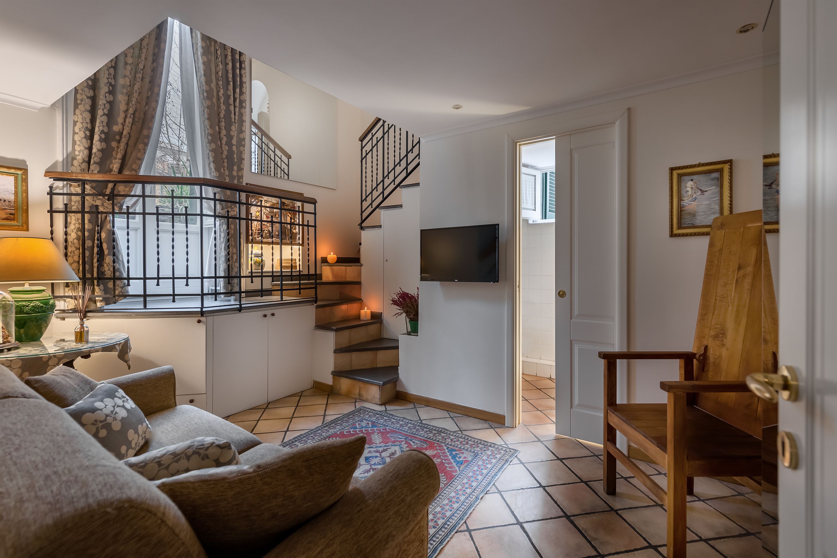 Un salon avec un canapé, une chaise en bois, un escalier et un téléviseur fixé au mur.