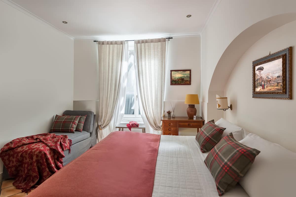 A hotel room with a bed, a desk, a chair, and a window with curtains.