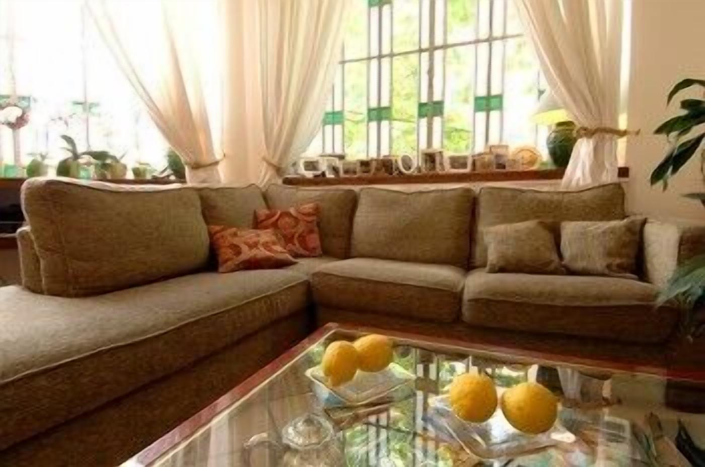 A living room with a sectional sofa, a glass coffee table with decorative items, and a window with curtains.