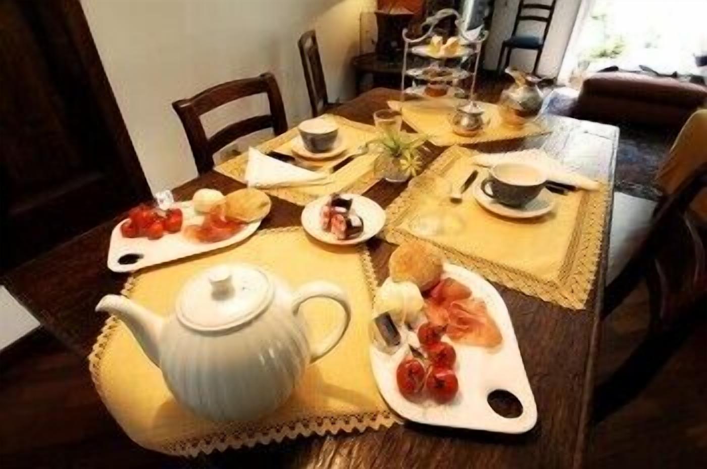 Una mesa de comedor dispuesta con platos de comida, una tetera y un frutero escalonado.