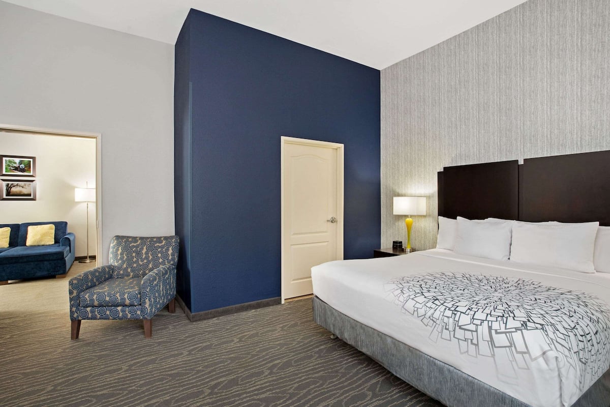 Ein Hotelzimmer mit einem großen Bett, einem blauen Sessel, einer Tür und einer Lampe.