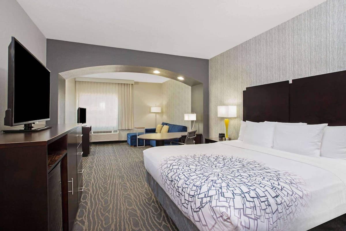 Ein Hotelzimmer mit einem großen Bett, einem Schreibtisch mit Flachbildfernseher, einer Couch und einem Esstisch.
