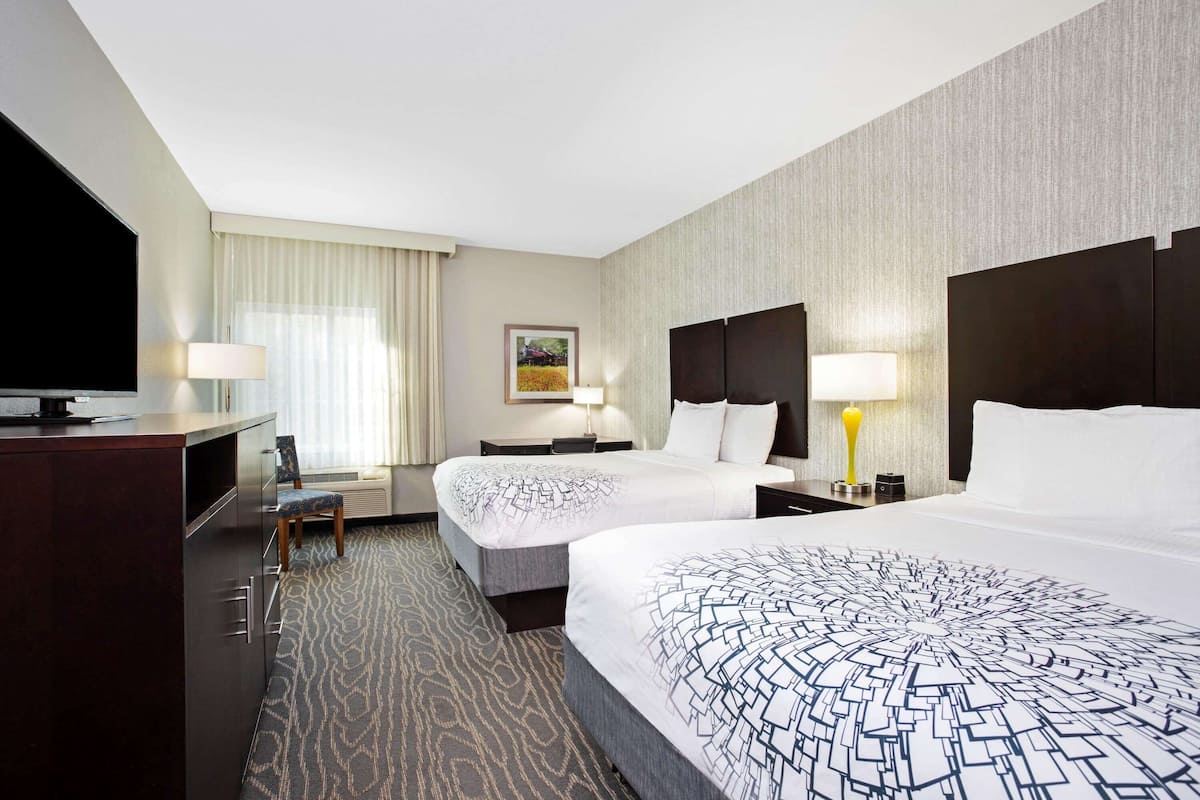 Ein Hotelzimmer mit zwei Betten, einem Schreibtisch, einem Stuhl und einem Fernseher.
