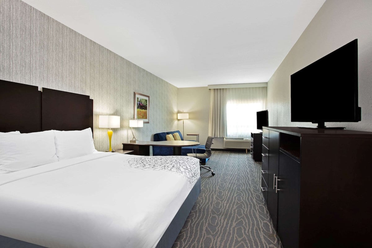 Ein Hotelzimmer mit einem großen Bett, einem Schreibtisch, einem Sessel, einem Fernseher und einem Kleiderschrank.