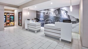 Un área de recepción moderna con un gran mural de un tren, mostradores de recepción blancos e interior bien iluminado.