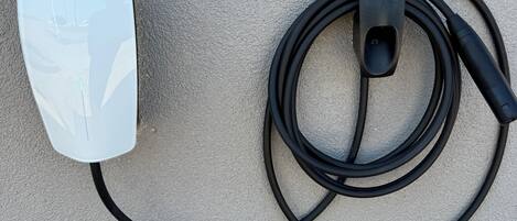 A Tesla charging station with a white charging unit and a black cable.