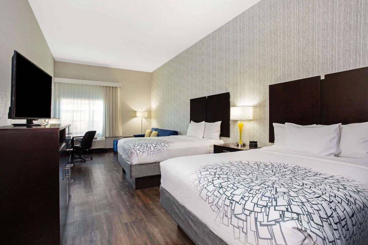Ein Hotelzimmer mit zwei Betten, einem Schreibtisch, einem Fernseher und einer Lampe.