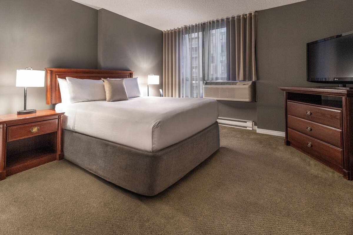 A hotel room with a large bed, a TV, a nightstand, and a dresser.
