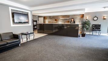 Un hall d’hôtel moderne avec un comptoir d’accueil, un téléviseur à écran plat, un canapé et une table basse.