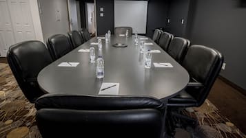 Une salle de conférence avec une longue table, des fauteuils en cuir noir, des bouteilles d’eau et un écran de projection.