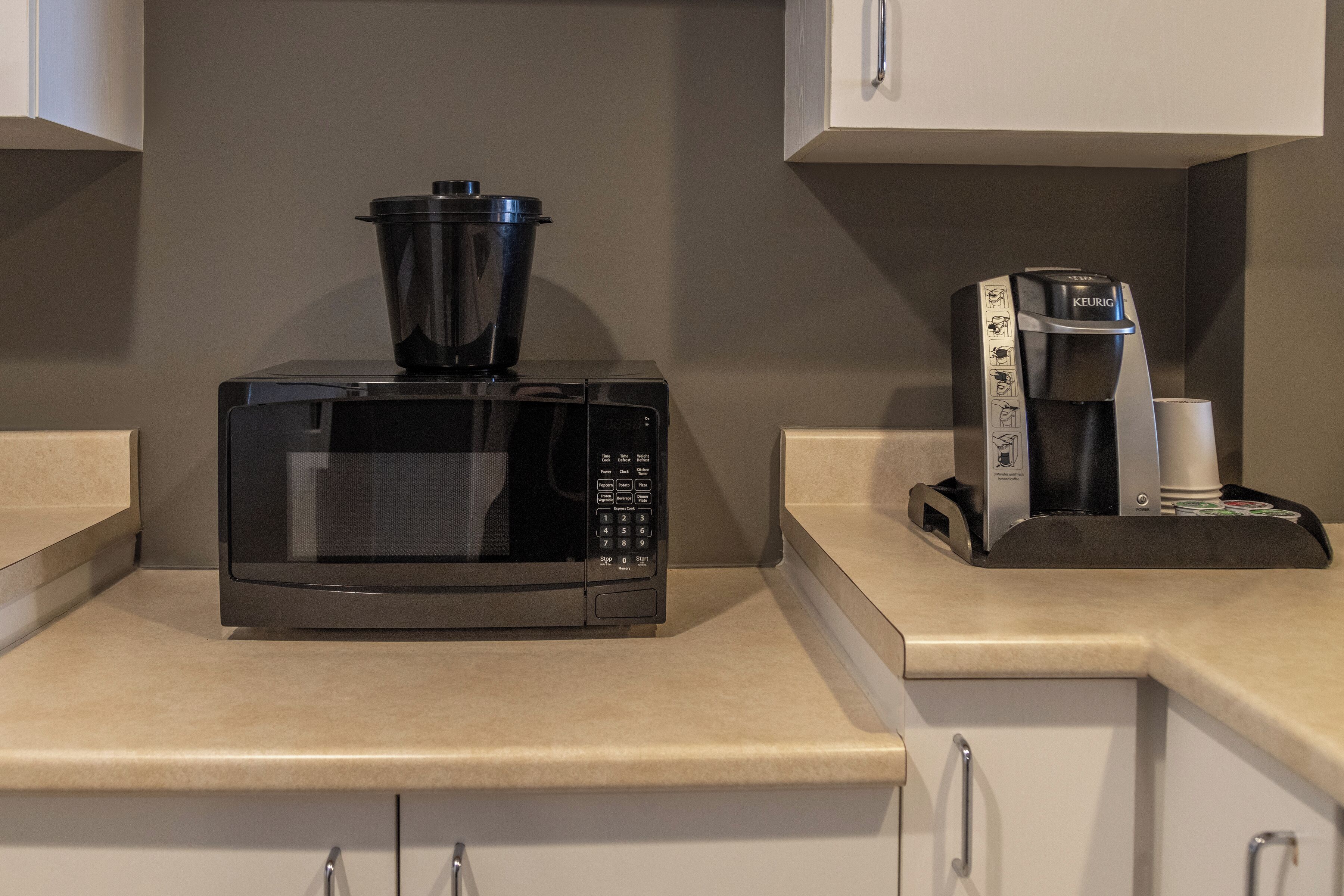 A kitchen with a microwave, coffee maker, and a black pot on the counter.