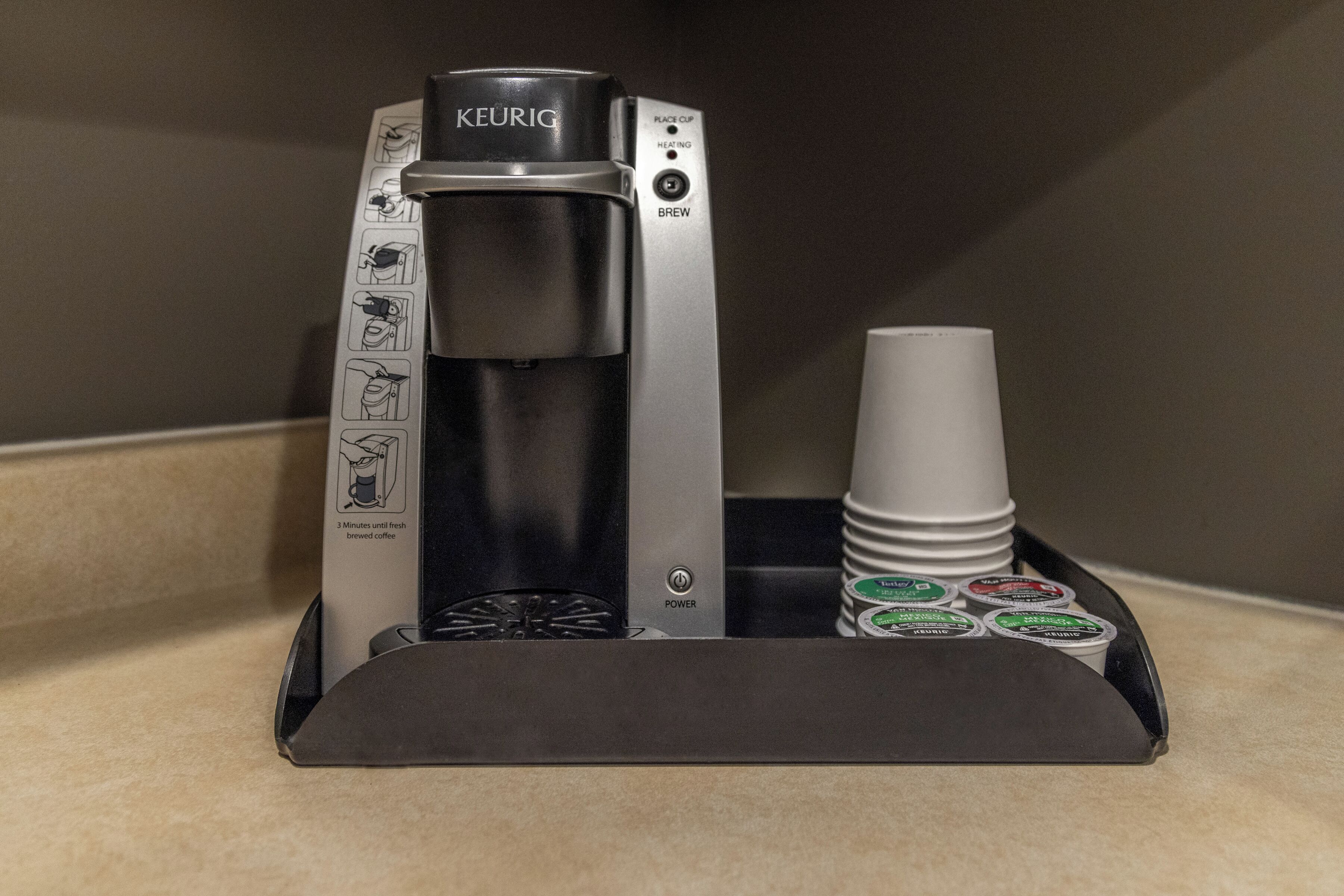 A Keurig coffee machine with a drip tray holding coffee pods and a disposable cup.