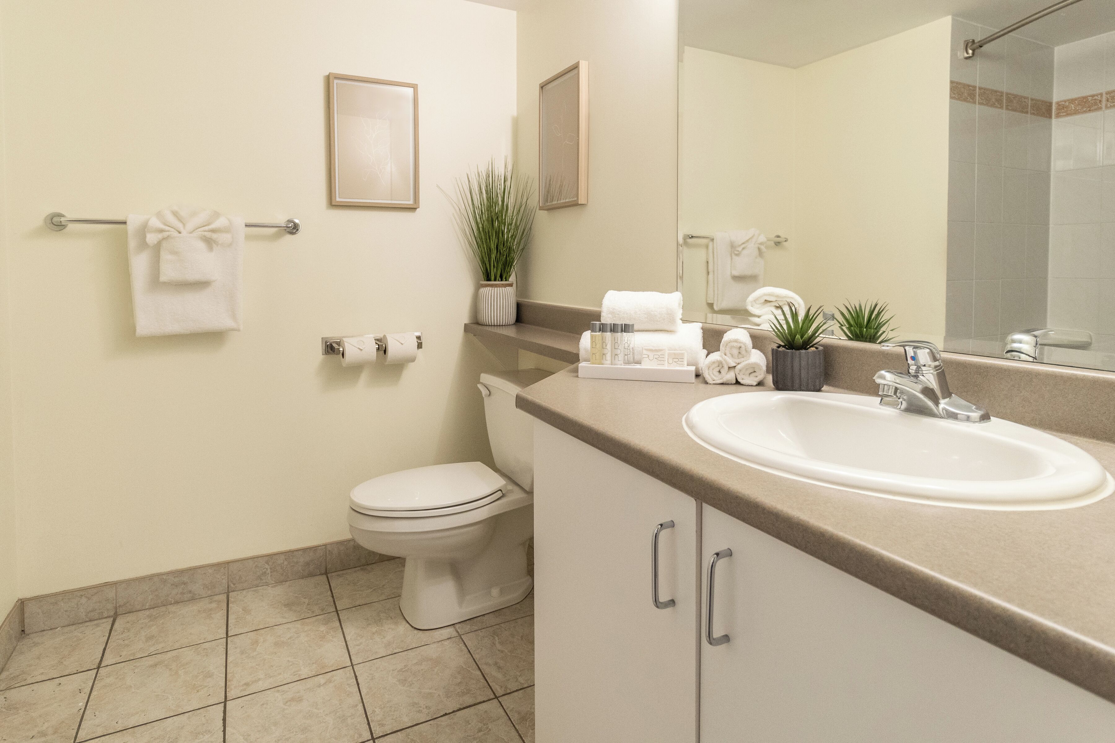 Un baño moderno con inodoro, lavamanos y espejo. Hay toallas y artículos de aseo en la encimera.