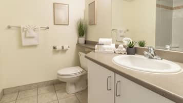 Un baño moderno con inodoro, lavamanos y espejo. Hay toallas y artículos de aseo en la encimera.