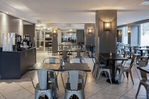 A modern dining area with multiple tables and chairs, a coffee station, and large windows providing natural light. - Hotel Faubourg Montreal (Montreal)