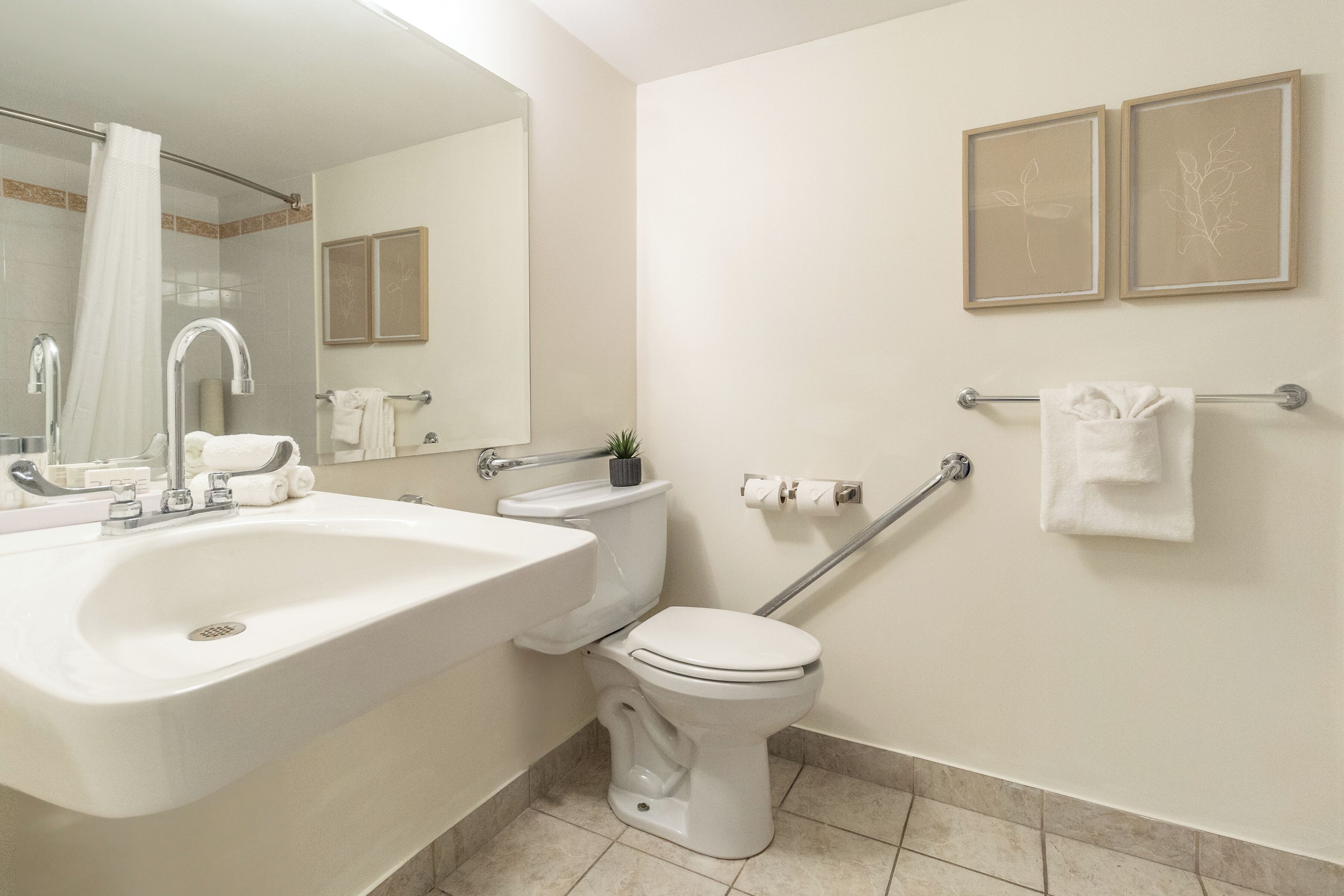 A bathroom with a white sink, toilet, and shower. There are two framed pictures on the wall and a towel rack with towels.