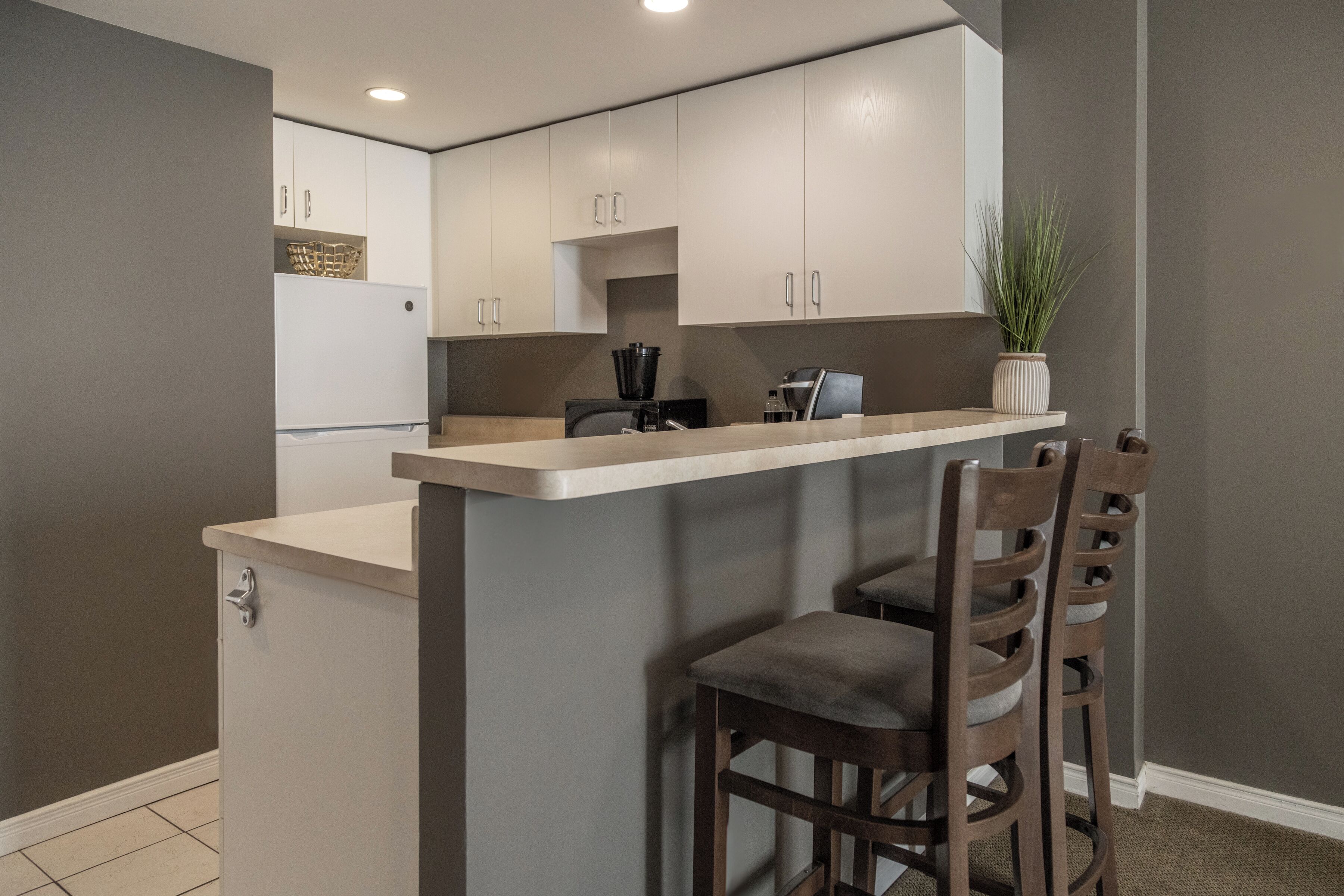 A compact kitchen with a central island, bar stools, and a potted plant.