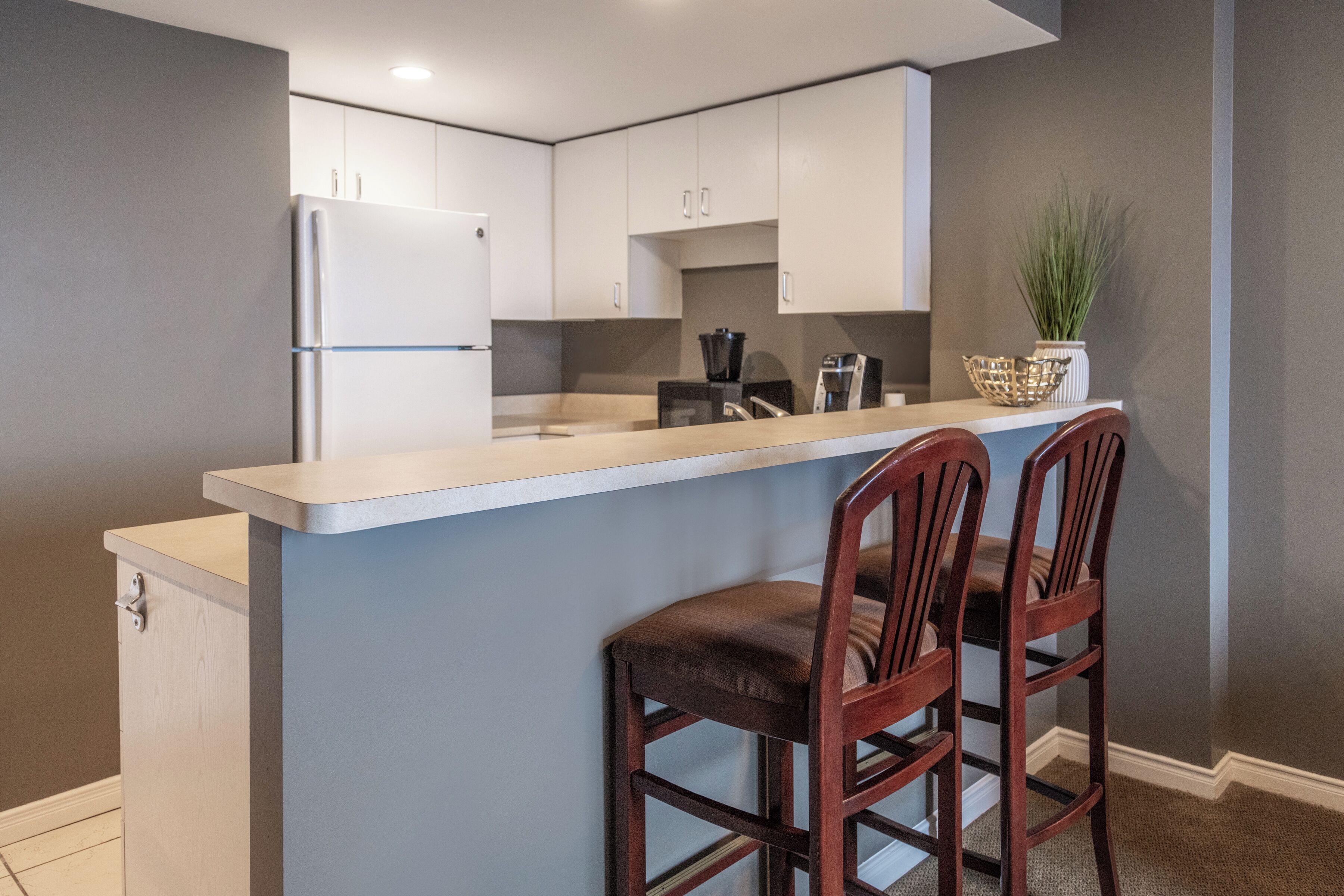 Une cuisine moderne avec des meubles blancs, un plan de travail de couleur claire et deux tabourets de bar en bois.