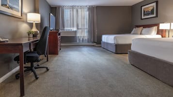 Quarto de hotel com escrivaninha, duas camas, uma cadeira, luminária, televisão e janela com cortinas.