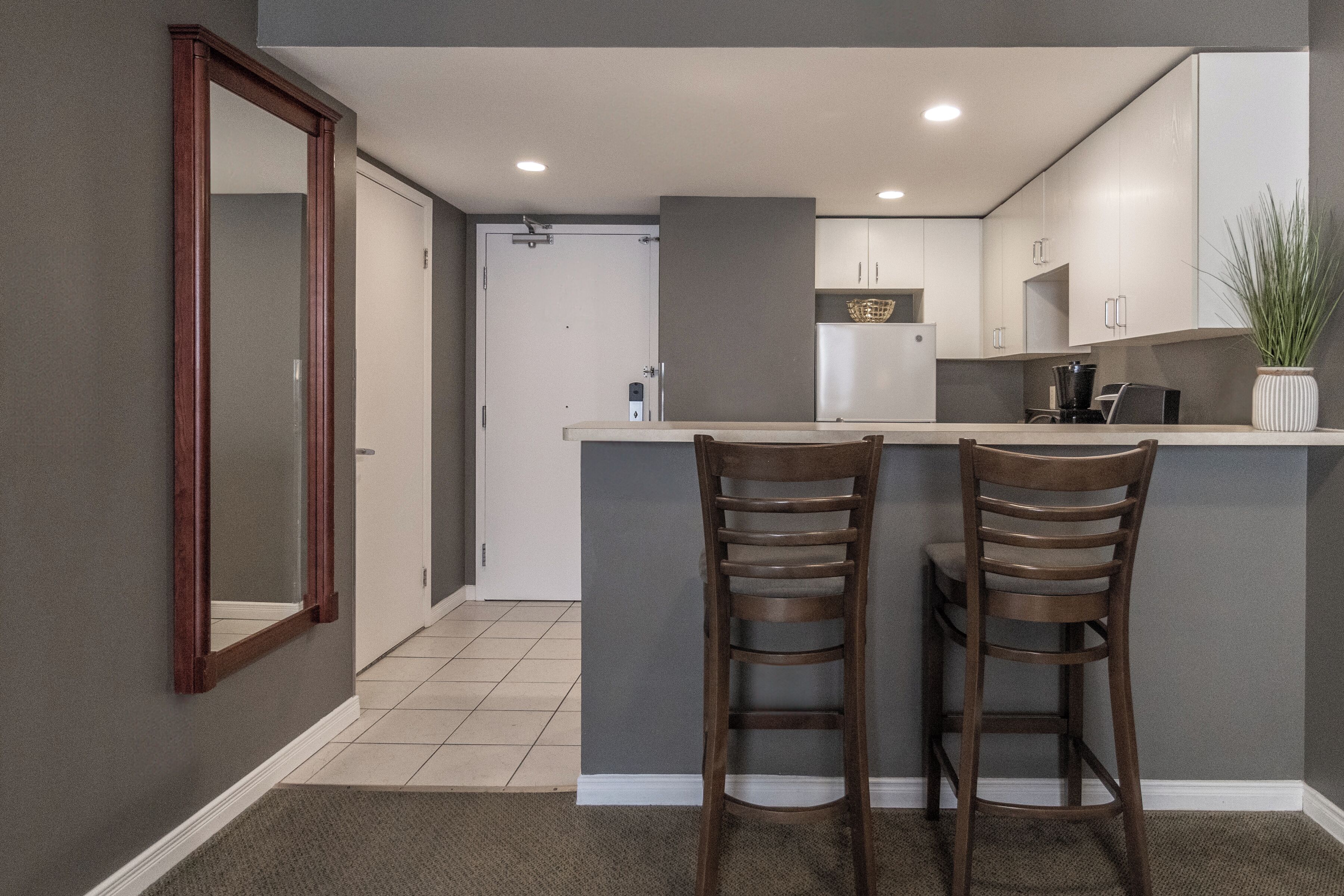 Cocina compacta con dos taburetes, un refrigerador y una planta en maceta.