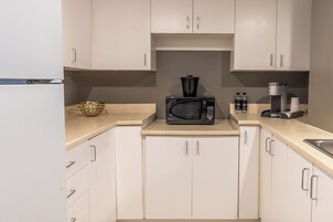 Une cuisine moderne avec des meubles blancs, un four à micro-ondes, une machine à café et un bol posé sur le plan de travail.