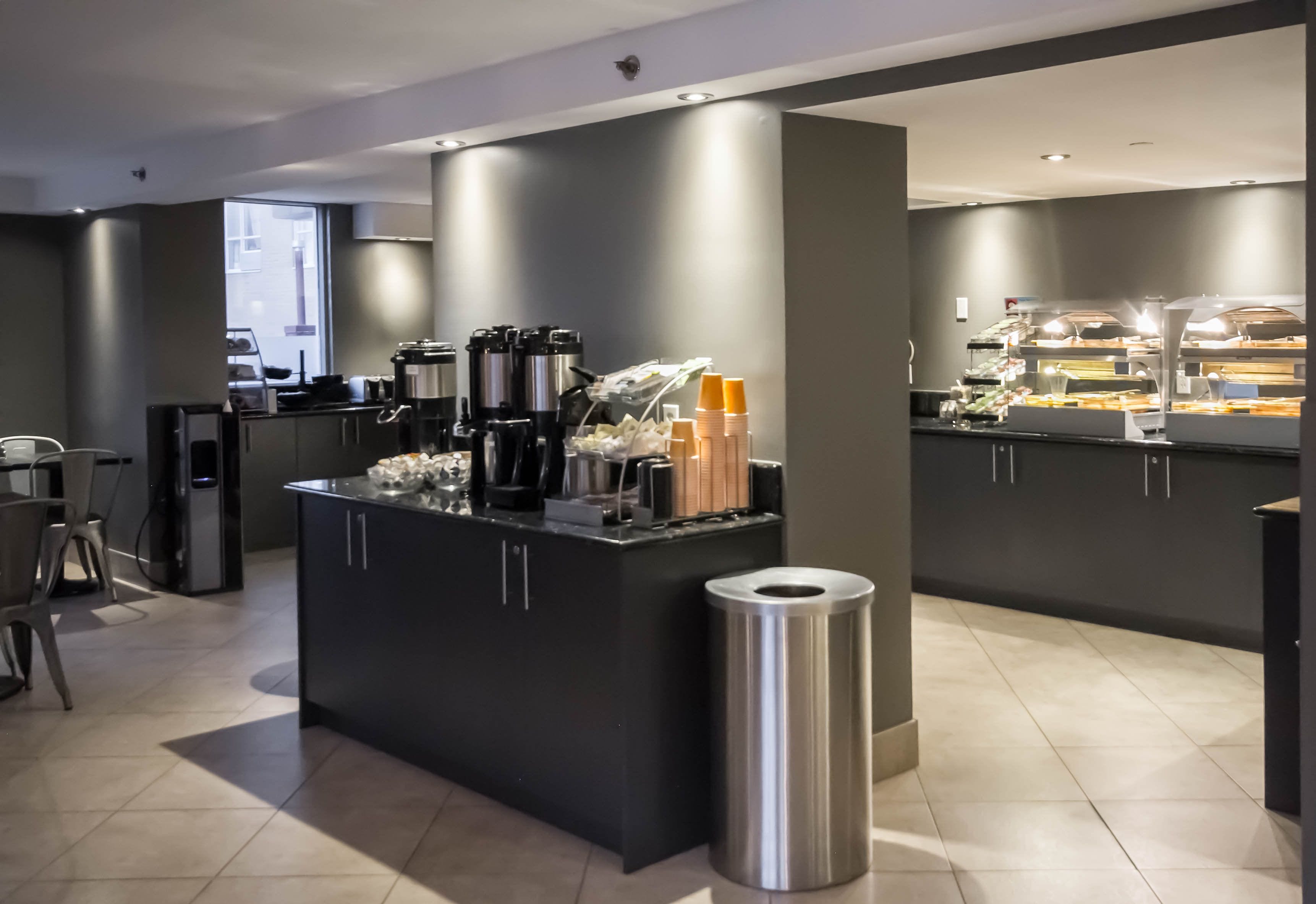 A modern kitchen area with a central island, coffee machines, and a trash bin.