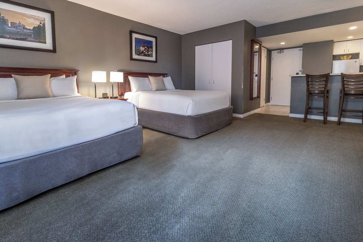 A hotel room with two beds, a kitchenette, and a dining area.