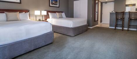 A hotel room with two beds, a kitchenette, and a dining area.