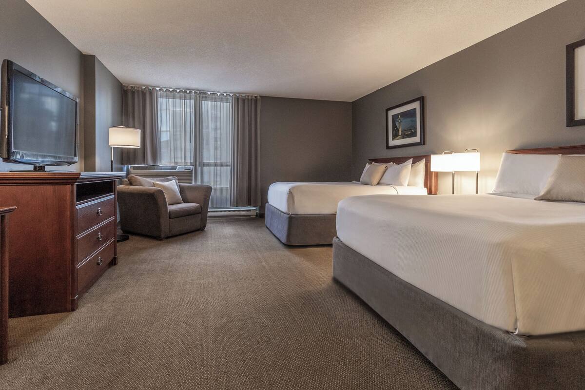 A hotel room with a flat-screen TV, a sofa, two beds, a desk, and a lamp.