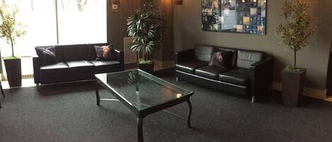 A modern lobby with two sofas, a glass coffee table, and potted plants.