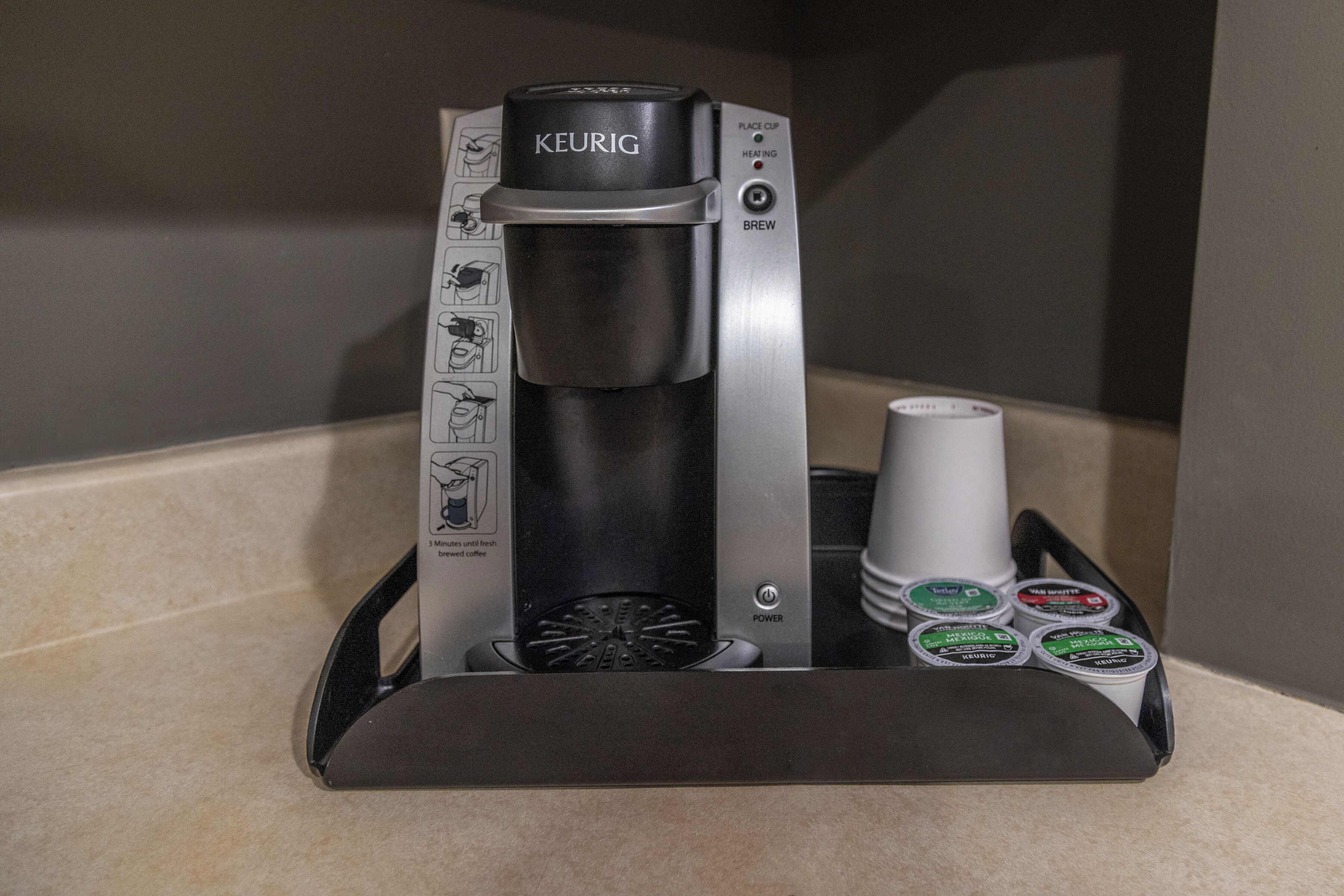 Eine Kaffeemaschine von Keurig mit Auffangtablett, Tassenhalter und vier Kaffeekapseln.